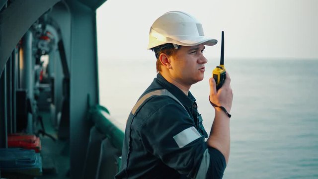 Marine Deck Officer or Chief mate on deck of vessel or ship . He holds VHF walkie-talkie radio in hands. Ship communication