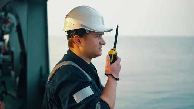 Marine Deck Officer or Chief mate on deck of vessel or ship . He holds VHF walkie-talkie radio in hands. Ship communication