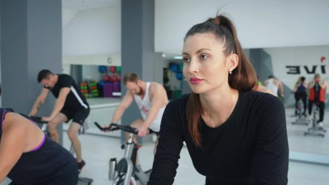 Beautiful focused woman cycling on spin bike at cycling class. Slow motion of athletic fit group in sportswear exercising on bikes in cycling class