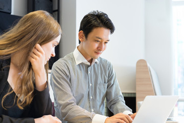 ノートパソコンで仕事をする男性と女性（人種の違う人々）