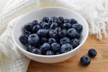 Bowl of fresh organic blueberries on rustic wooden table draped