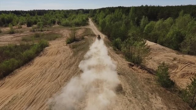 Slow-motion video of a man riding a yellow quad bike, and speeding off into the distance, leaving behind a cloud of dirt and dust
