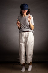 a young woman in a light t-shirt, trousers and blue cap poses on a dark background