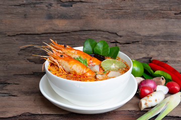 Tom Yum Goong or Shrimp soup spicy sour Soup Traditional food in Thailand contains chili, lime,lemongrass, lime leaf, along with cooked rice in a white dish on the old wood background.