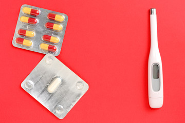 Thermometer and silver blisters with pills on a red background. Pharmacy and medical concept. Flat lay, top view