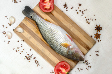 Fresh and clean bass with tomato, garlic, pepper, star anise on the chopping board