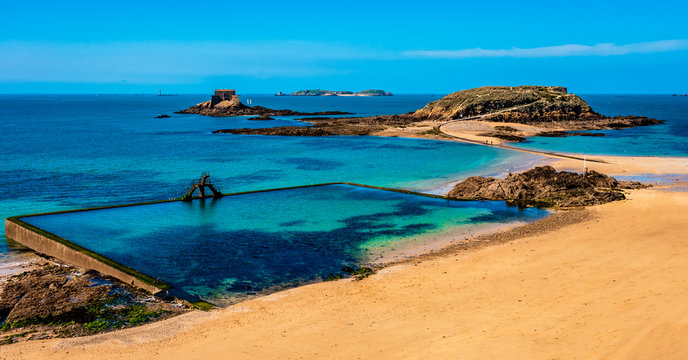 Saint Malo in Brittany, France overlooking the beach, natural pool and fort islands on a sunny day with green waters and golden sand.