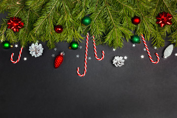 Christmas border from fir branches, decorations and candy canes on black background.