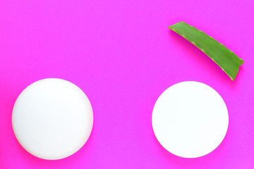 Aloe vera fresh leaf and white jars of cream on a bright pink background. Organic cosmetics with natural ingredients. Top view, copy space