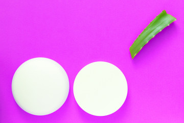 Aloe vera fresh leaf and white jars of cream on a bright pink background. Organic cosmetics with natural ingredients. Top view, copy space