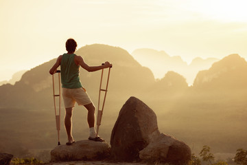 Injured man stands with crutches on big rock