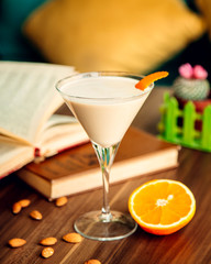 milky cocktail garnished with orange zest in martini glass