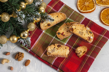 Traditional Italian Biscotti or Cantuccini cookies with hazelnuts, almonds, walnuts on a red-green napkin near the Christmas tree. Christmas and New Year baking. Top view