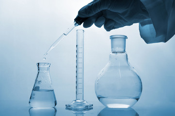 hand of scientist dropping water in glass science flask with cylinder in blue medical science laboratory