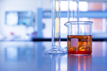 glass beaker with orange solution and cylinder in blue chemistry laboratory background