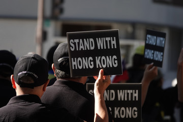 Signs reading STAND WITH HONG KONG are shown being held from behind unidentified men wearing hats embroidered with CHINA DEMOCRACY PARTY in English on the back.