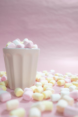 Cup full of tiny colored marshmallows and a lot of marshmallows on the table surface