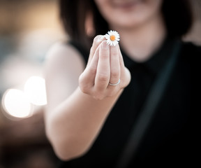 Hand of girl holding and giving a flower with bokeh (blurred) background.