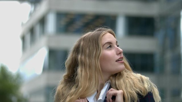 close up of young student/businesswoman behind building looking intently around with confidence and a big smile
