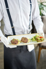 The waiter is holding a plate Delicious juicy meat cutlets, mashed potatoes sprinkled with greens and fresh healthy salad of tomatoes and lettuce leaves.