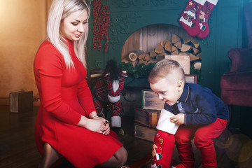 lovely mother and cute baby boy near christmas decorations and ski.a child getting present from the red stocking