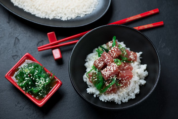 Poke bowl with tuna fillet, white rice and chuka, elevated view over black stone background, studio shot