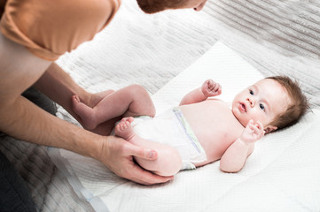 Young dad changes the diaper for his baby. White background. Close-up. Newborn care concept.