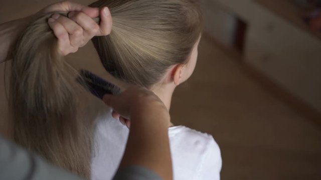 grandmother combs granddaughter teenager long blonde hair and makes ponytail using white band upper view