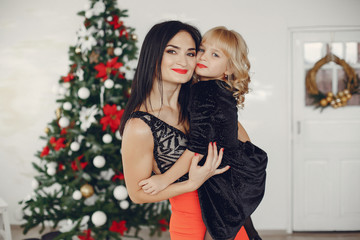 Beautiful mother in a black dress. Cute little girl near christmas tree