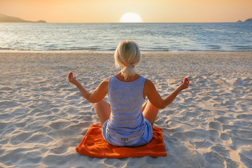 Woman practicing yoga on sea beach during sunset. Beautiful yoga background.
