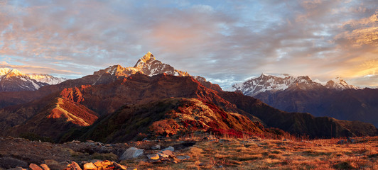 Panoramic view of the majestic Himalayan peaks - Machapuchare, Annapurna IV and Annapurna II, covered with clouds illuminated by the sunset. View from the Korchon mountain shelter.