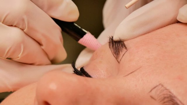 Beautician makes eyebrow correction to his patient. Marking the contour of the eyebrows with a special pencil