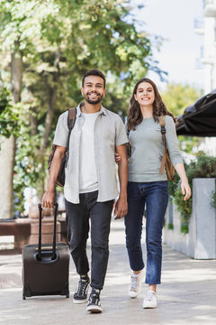 Happy young couple travelers walking around the city with luggage. Two beautiful smiling lovers travelling europe. Love, travel, tourism, vacation and active lifestyle concept