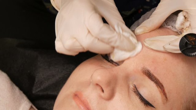 The cosmetologist removes the remains of the coloring pigment from the skin of the eyebrows with a special napkin.