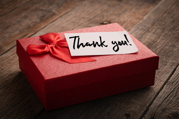 Red gift box and label with the words thank you on a wooden background: concept of expressing...