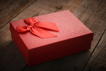 Gift box of red color with a red ribbon on the lid on a wooden background as a concept of gift and romantic gift