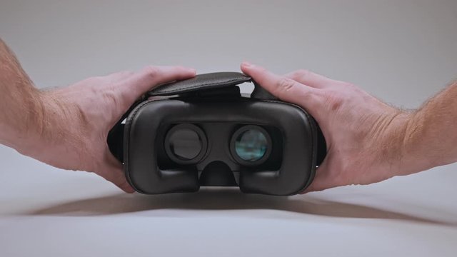 Man's hands take vr glasses and wear them at white background. Male hands holding VR headset. Virtual reality mask. Close-up in 4K, UHD