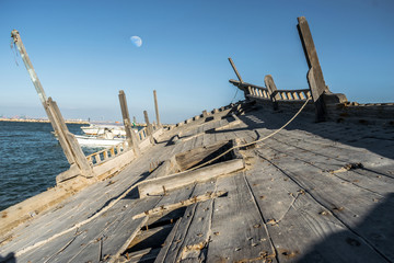 an abandoned broken old wooden boat at a beach and other speed modern boats in the background and...