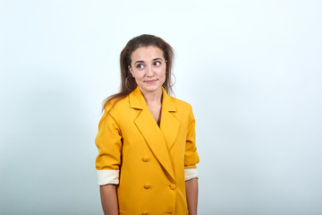 Cheerful young woman in yellow jacket looking aside, smiling isolated on gray background in studio. People sincere emotions, lifestyle concept.