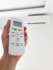 Modern airconditioner unit with a hand holding a remote.