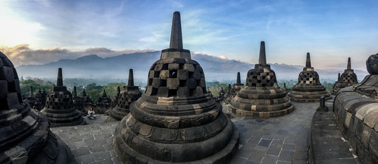 Woman meditating Panorama of Borobudur sacred temple, stuning ancient temple with black stone bells (stupa) in yogyakarta, java, indonesia