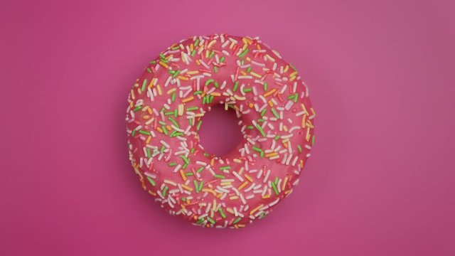 Delicious pink donut with colorful sprinkles rotating at pink background. Top view of colorful doughnut spinning. Food concept. Close-up in 4K, UHD