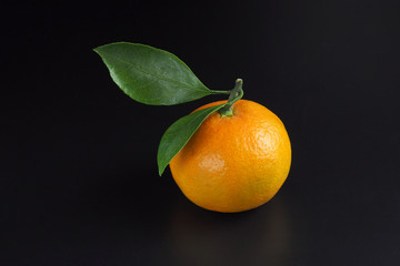 Yellow ripe mandarin with green leaves on a black background