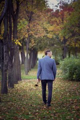 slender young stylish trumpeter walking through alley in autumn park