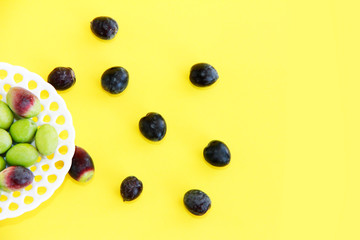 natural round green and brown olives in a decorative plate on a yellow background