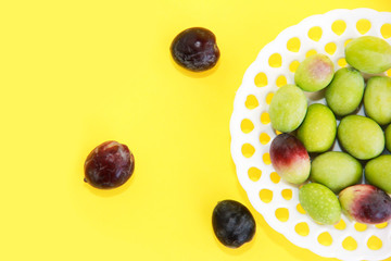 natural round green and brown olives in a decorative plate on a yellow background