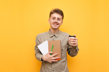 Happy student in shirt, mustache and glasses stands on yellow background, holds a notebook, books...