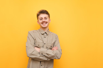 Smiling nerd in shirt and glasses stands on yellow background and poses at camera. Portrait of cheerful student with mustache and smile on face isolated on yellow background. © bodnarphoto
