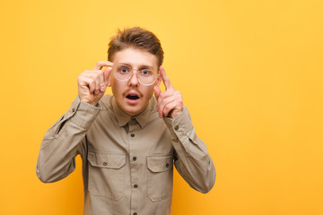 Bad-eyed, bewildered man looks into the camera and adjusts his glasses, wears a shirt and mustache. Funny surprised nerd looks intently at the camera against a yellow background. Isolated.