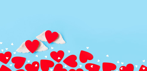 Valentine's Day concept background. Two red hearts with angel wings and confetti on pastel blue background. Flat lay, top view, copy space